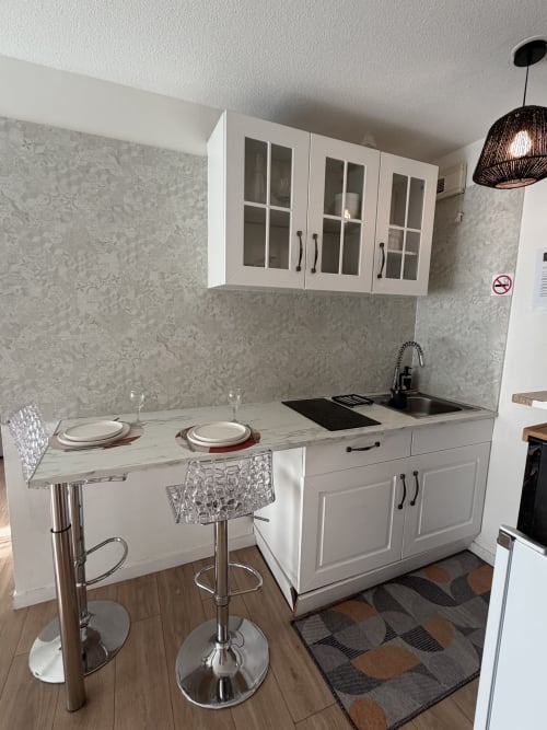 Kitchenette moderne aux armoires blanches, plan de travail en marbre et bar de cuisine à l'appartement Appart'NoOm en France