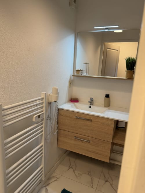 Salle de bains moderne d'Appart'NoOm avec vanité en bois, grand miroir, sèche-serviettes chauffant et carrelage en marbre
