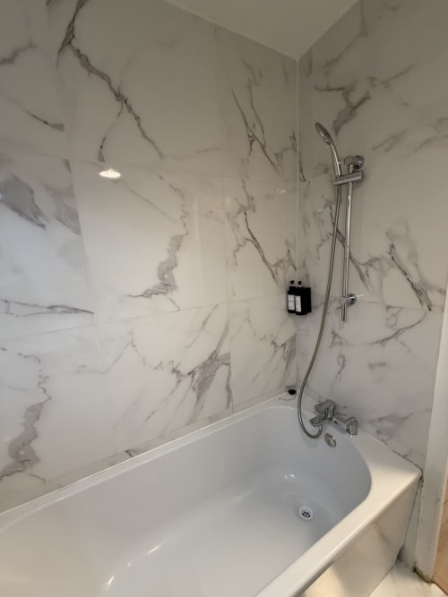 Salle de bain moderne en marbre avec baignoire blanche, douchette chromée et distributeur de savon noir à Appart'NoOm