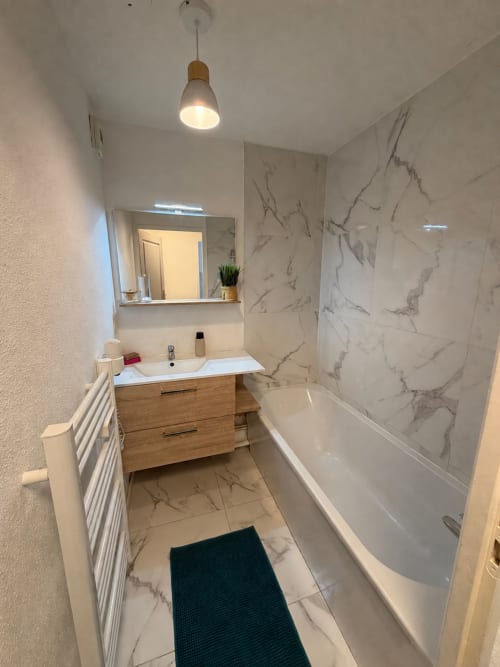 Salle de bain moderne chez Appart'NoOm avec carrelage marbre, meuble vasque en bois, baignoire blanche et éclairage suspendu