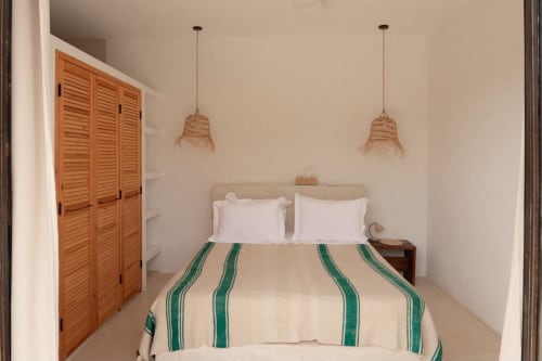 Chambre beige au Domaine Belhazar à Essaouira avec linge de lit rayé, luminaires suspendus tissés et portes de placard en bois