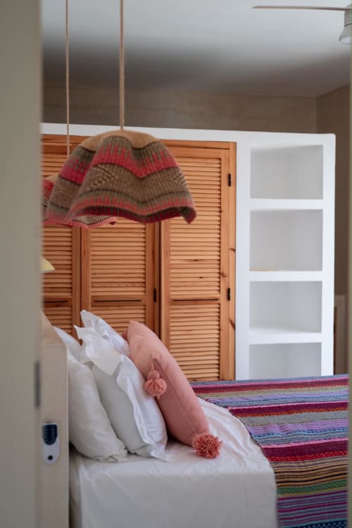 Chambre à Domaine Belhazar à Essaouira avec literie rayée colorée, oreillers blancs, coussins roses et bonnet tricoté rayé