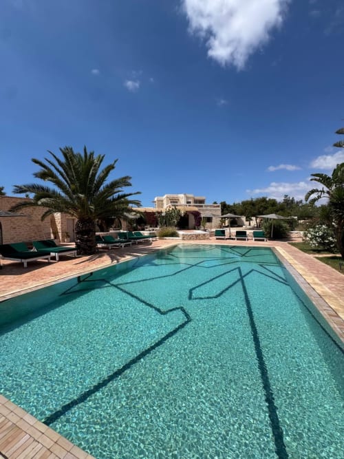 Piscine aux eaux cristallines avec couloirs délimités à la villa de luxe Domaine Belhazar à Essaouira, Maroc, entourée de palmiers