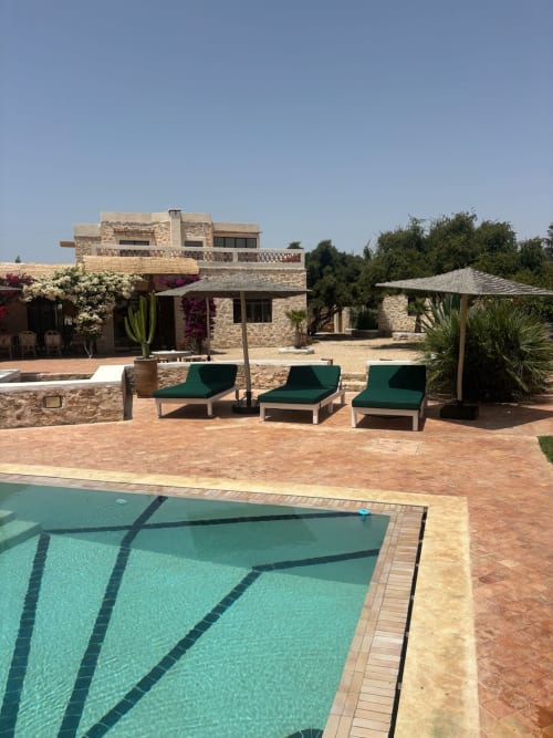 Piscine et espace détente du Domaine Belhazar à Essaouira avec bassin turquoise, transats verts et bâtiments en pierre