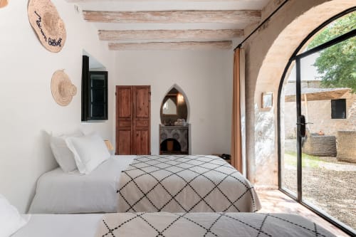 Chambre lumineuse avec lits jumeaux, poutres en bois, arche et vue sur la cour du Domaine Belhazar à Essaouira