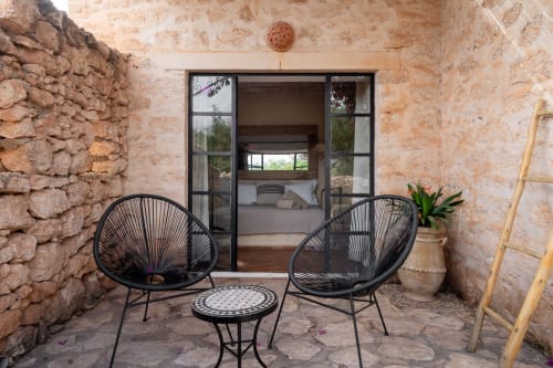 Coin détente à Domaine Belhazar à Essaouira avec chaises noires, petite table et murs en pierre