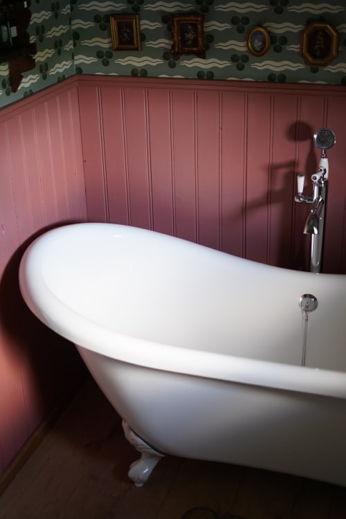 Baignoire ancienne à pieds griffus dans la chambre Meadow de La Roquerie, Normandie, avec lambris mauve et motifs