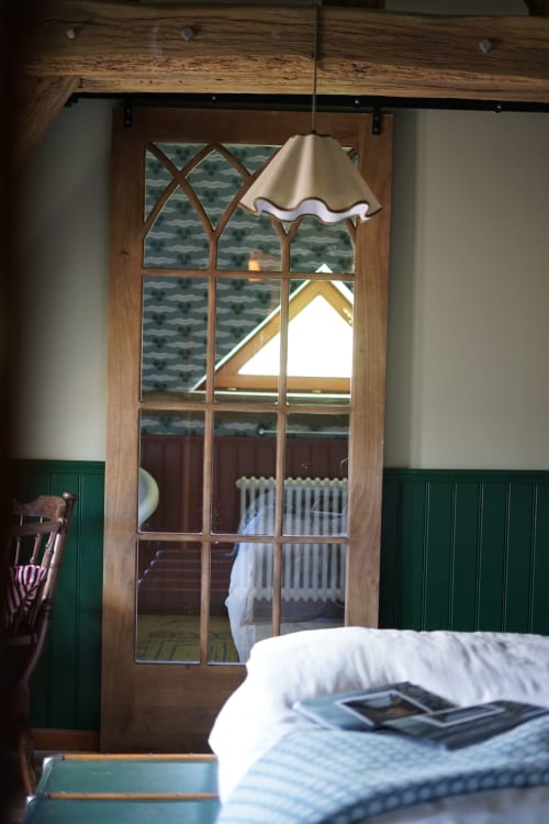 Chambre douillette de la Ferme La Roquerie avec porte en bois, lampe suspension crème et vue sur le jardin en Normandie