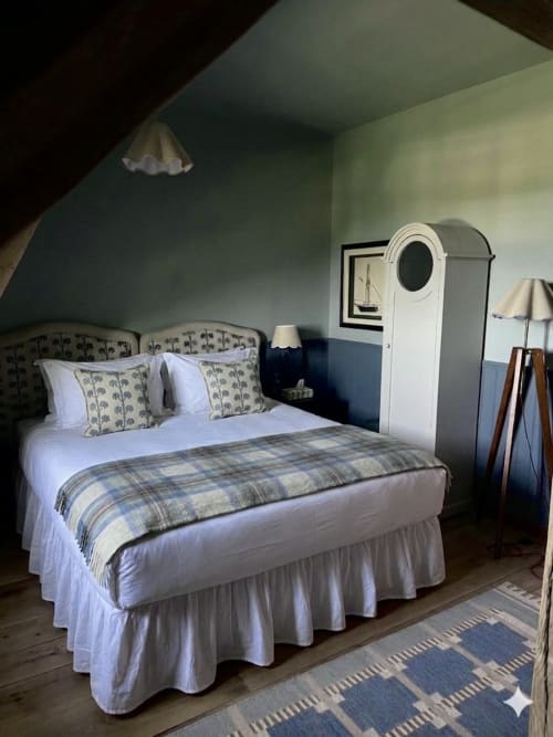 Chambre chaleureuse de la Ferme La Roquerie avec literie écossaise, tête de lit ornementée et décor rustique fermier français