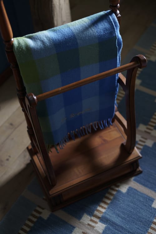 Couverture en laine aux rayures bleues et vertes drapée sur un portant en bois dans la chambre Paddock de la Ferme La Roquerie