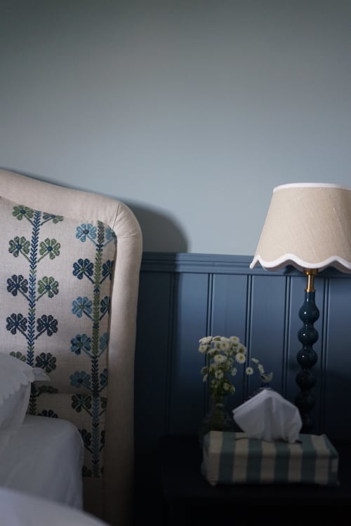 Chambre Paddock à la Ferme de La Roquerie avec tête de lit capitonnée, lampe de chevet et fleurs frais