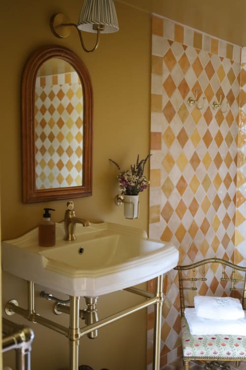 Salle de bain élégante à la Ferme La Roquerie avec lavabo vintage sur piédestal, robinetterie en laiton et carreaux à motifs géométriques losange