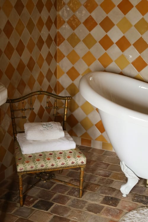 Coin élégant de salle de bain à La Roquerie avec carrelage géométrique, baignoire blanche et fauteuil décoratif
