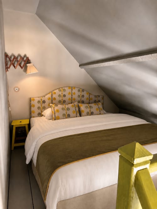 Chambre mansardée cosy à La Roquerie avec tête de lit motifs, draps blancs, touches jaunes et plafond en pente