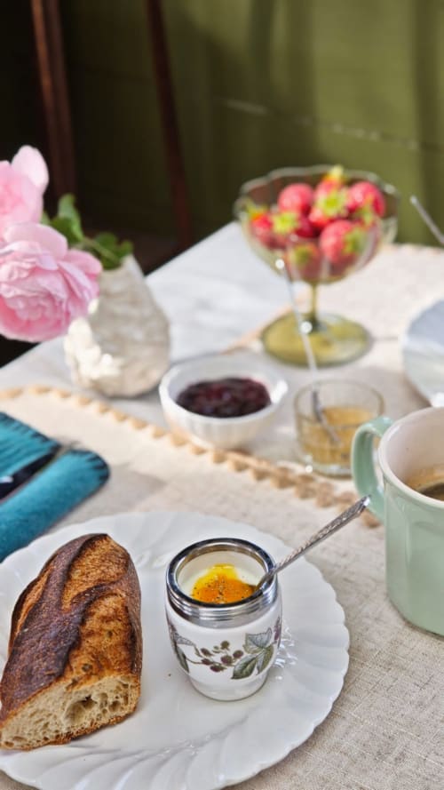Table de petit-déjeuner élégante à La Maison 1903 avec pain frais, confiture, fraises, fleurs roses et café à Trévou-Tréguignec