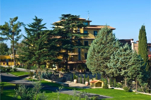 Villa gialla del Green Hotel Poggio Regillo a Frascati circondata da cipressi e giardini curati sotto un cielo azzurro.