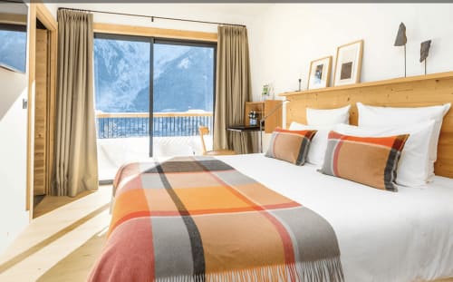 Deluxe bedroom at Le Chalet Mont-Blanc with mountain views, wooden bed, plaid throw, and balcony overlooking snowy Alps