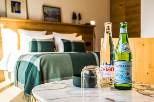 Deluxe bedroom at Le Chalet Mont-Blanc with beverages on marble table and green-accented bedding in Les Houches