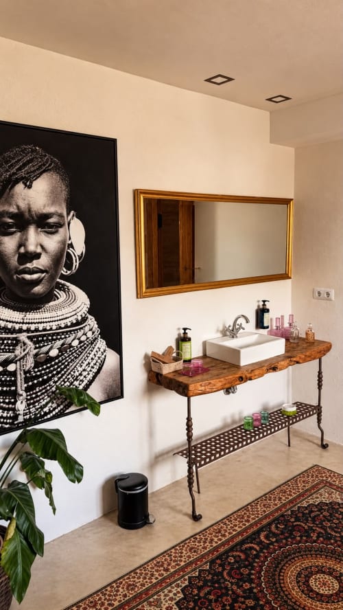 Modern bathroom at Finca Almenara De Copau hotel in Zaragoza with wooden vanity, gold mirror, and African portrait art.