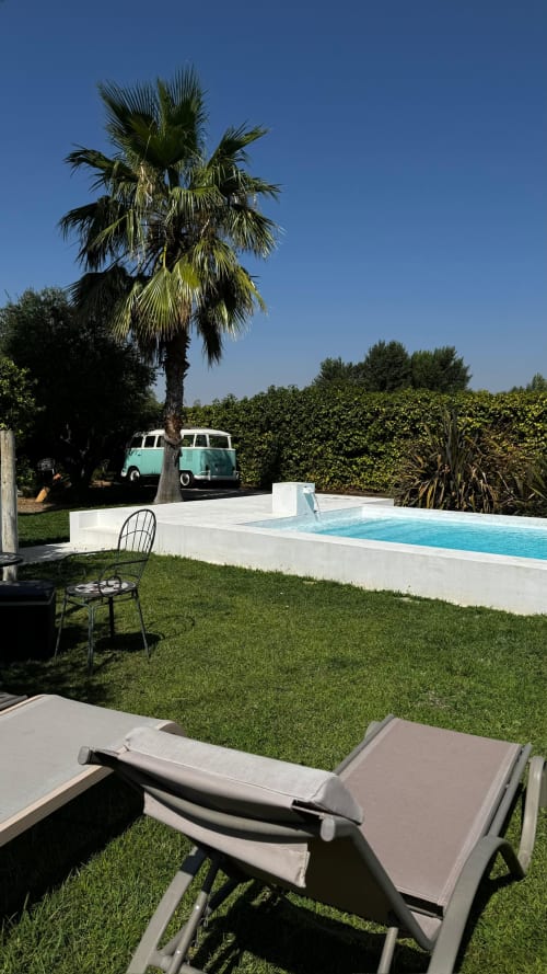 Finca Almenara De Copau pool view with loungers, palm tree, turquoise van, and manicured gardens under clear sky