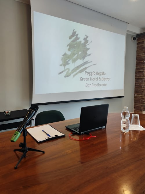 Sala conferenze dell'hotel Poggio Regillo Green a Frascati con schermo per presentazioni che mostra il branding dell'hotel e il bistrot