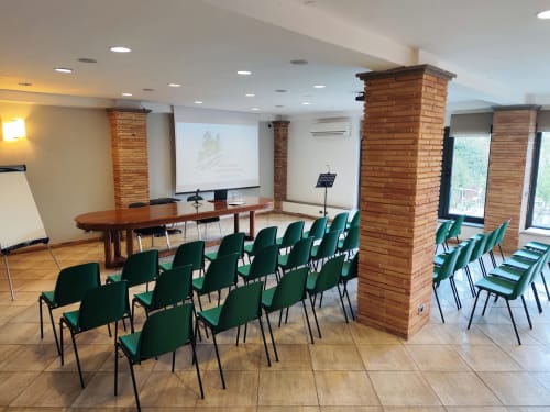 Sala conferenze Green Hotel Poggio Regillo a Frascati con sedie verdi, tavolo in legno e colonne in mattoni.