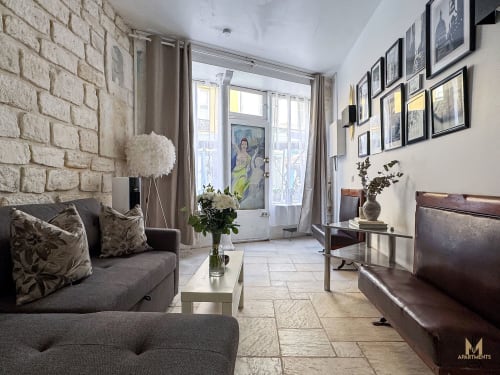Modern Montmartre apartment living room with stone walls, gray sofa, leather seating, and French doors opening to balcony in