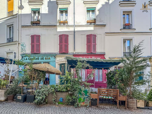 Charming Montmartre street with cafes, colorful storefronts, and flowering planters in Paris