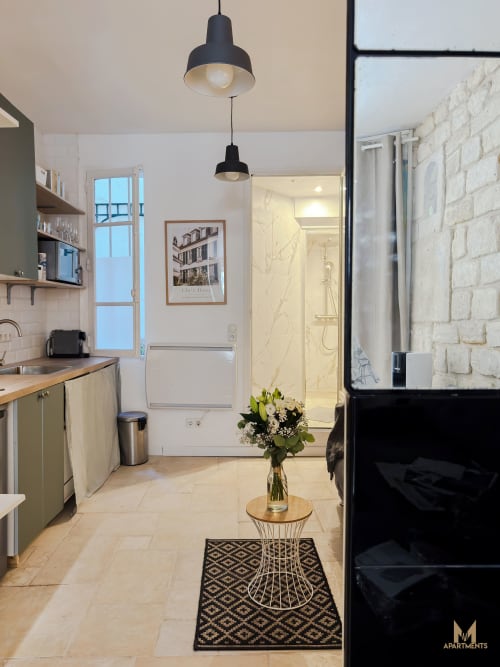 Modern Paris apartment kitchen with black pendant lights, marble bathroom, white brick wall, and fresh flowers in Montmartre