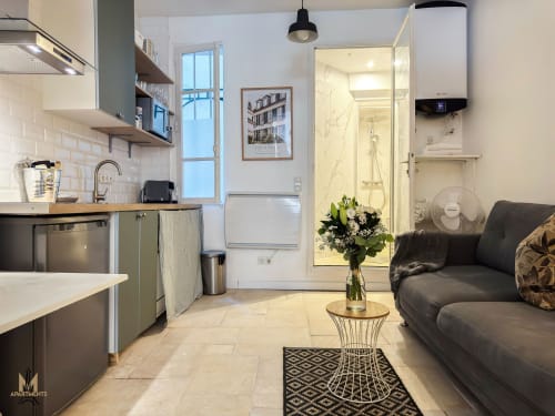 Modern studio apartment in Paris Montmartre with open-plan kitchen, living area, black sofa, and marble bathroom entrance.
