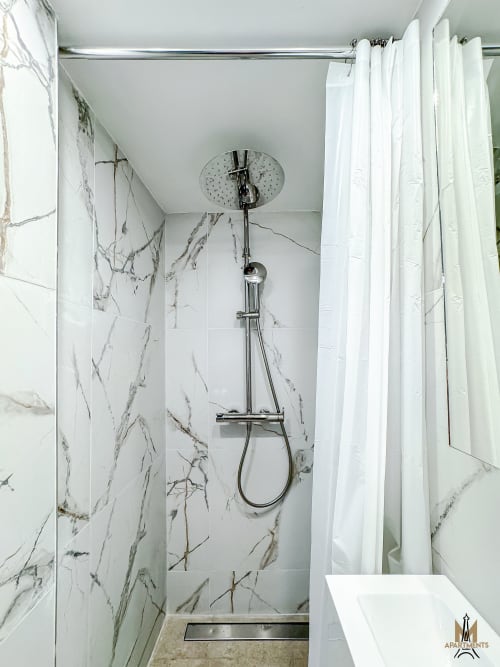 Modern shower at Montmartre Apartments Paris featuring marble-effect tiles, rainfall showerhead, and white curtain