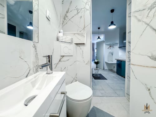 Modern bathroom in Montmartre Apartments, Paris with marble walls, white vanity, and black pendant lights