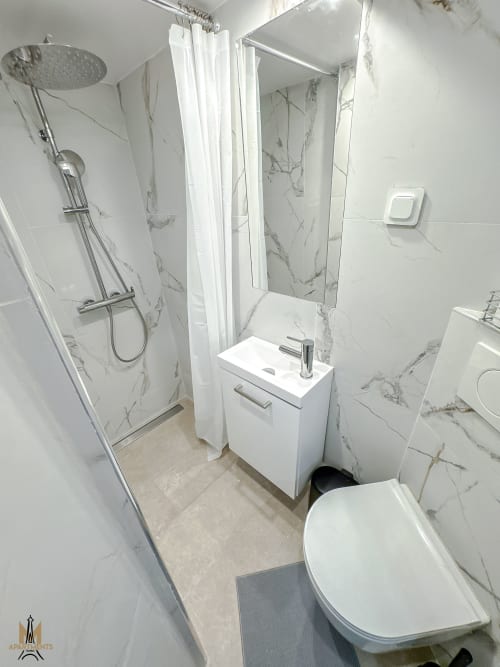Modern bathroom in Montmartre Apartments Paris with marble tiles, rainfall shower, white vanity, toilet, and mirror