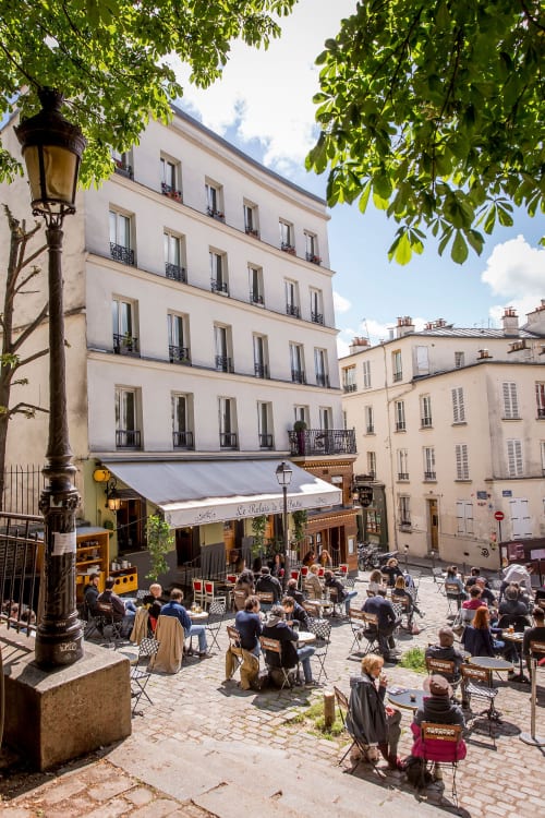 Charming Montmartre square in Paris with outdoor café seating, historic Parisian buildings, and green foliage