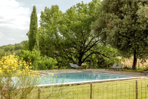 Piscina di hotel toscano con lettini, cipressi e terrazza in pietra a Buonconvento