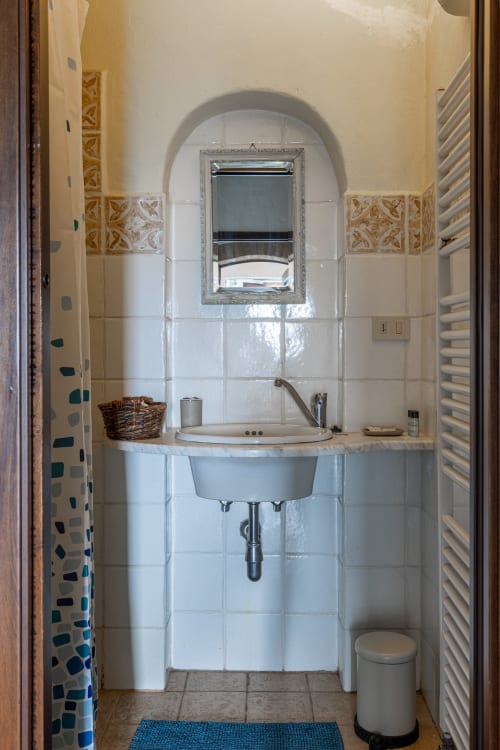 Bagno della camera Cipresso presso SOC AGR QUARANTALLINA a Buonconvento con piastrelle bianche, specchio ad arco e lavabo rotondo