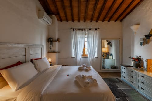 Camera Cipresso in hotel Buonconvento con letto bianco, travi in legno a vista e pavimenti in cotto.