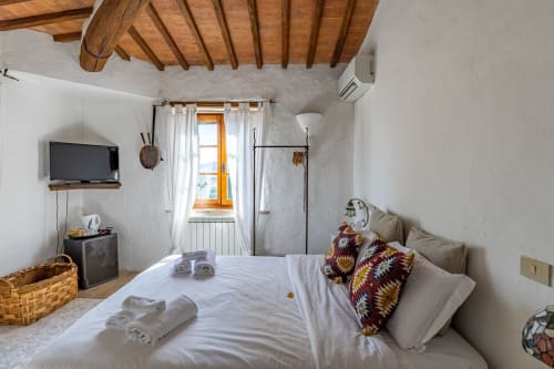 Camera luminosa Olmo all'hotel Quarantallina di Buonconvento, con soffitto in travi di legno, pareti bianche e letto