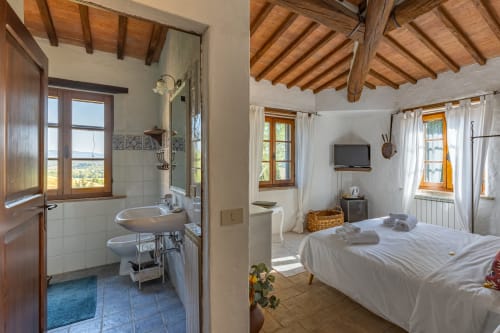 Camera da letto rustica con bagno ensuite, travi in legno e vista sulla campagna toscana presso l'hotel Quarantallina