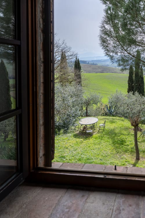 Vista sulla campagna toscana dalla camera Olmo dell'hotel Quarantallina a Buonconvento, con tavolo in giardino e dolci colline verdi