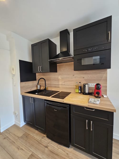 Cuisine moderne noire avec plan de travail et crédence en bois au Studio Mirabeau 2 des Lodges de Barbieux, Croix