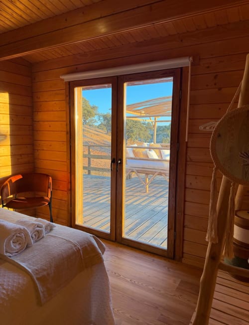 Quarto ensolarado em villa de madeira com portas de vidro que abrem para terraço e vista de piscina em Corvatos Casas do Monte, Almodôvar