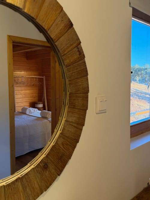 Espelho com moldura de madeira refletindo quarto com toalhas enroladas na vila Corvatos Casas do Monte em Almodôvar