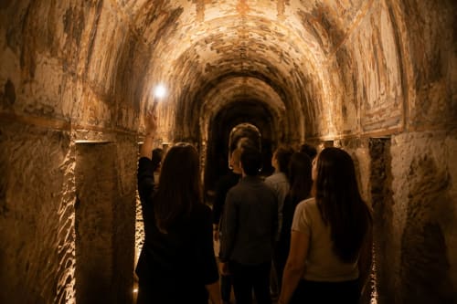 Tourists exploring ancient stone tunnel in Rome with warm lighting