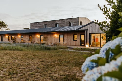 Cottage moderne en bois aux Écuries du bout du monde à Landunvez, terrasse illuminée et vue jardin au crépuscule