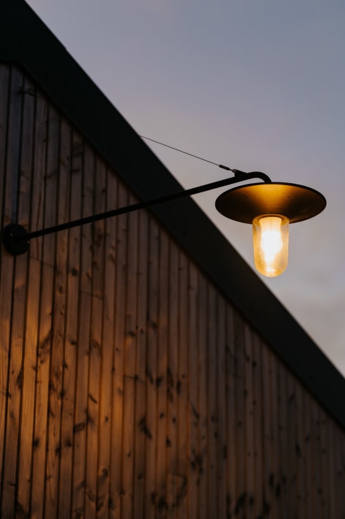 Applique murale illuminée sur bâtiment en tôle ondulée au crépuscule, gîte Les écuries du bout du monde, Landunvez