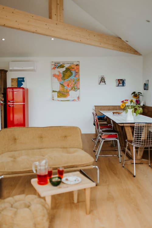 Séjour lumineux aux Écuries du bout du monde avec poutres en bois, réfrigérateur rétro rouge et coin repas