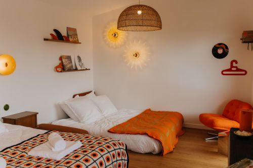 Chambre douillette aux Écuries du Bout du Monde avec lits jumeaux, touches orangées et lampe suspendue tressée à Landunvez