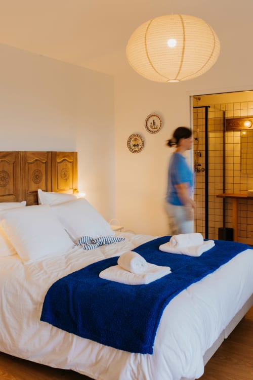 Chambre douillette du gîte Les écuries du bout du monde à Landunvez avec plaid bleu, tête de lit en bois et lampe de plafond ronde