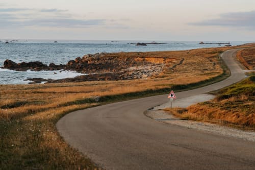 Route côtière sinueuse avec panneau d'avertissement près de Landunvez, Bretagne, surplombant des rivages rocheux et la mer